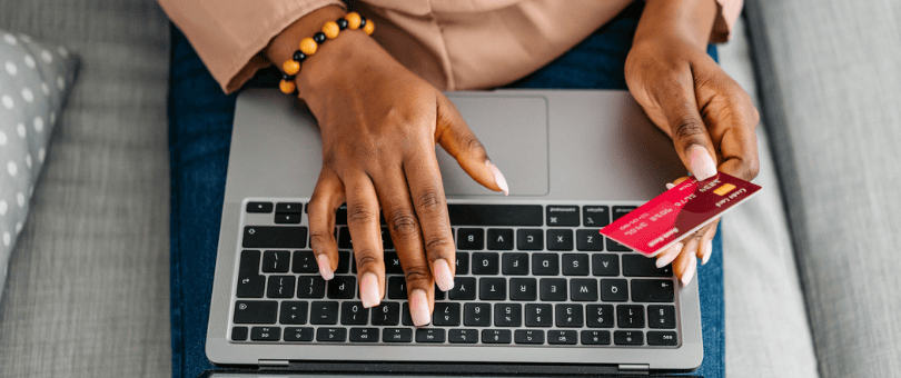 Woman with one hand on laptop keyboard and the other holding a credit card for a blog post about AMEX CID Chargeback Policy