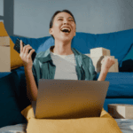 A woman gleeful at her laptop amid piles of boxes from ecommerce orders — to illustrate malicious friendly fraud and gaps in AI fraud detection.