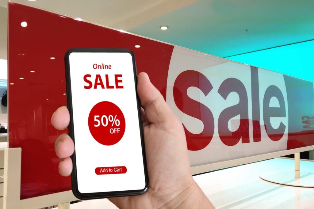 shopper with a mobile device displaying 50% off sale in forefront of big "Sale" sign.