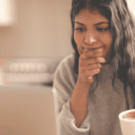 A woman shopping online in her kitchen with coffee, seriously considering a purchase