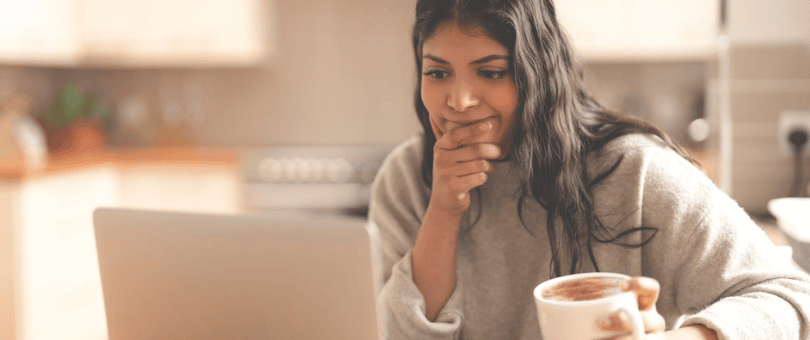 A woman shopping online in her kitchen with coffee, seriously considering a purchase