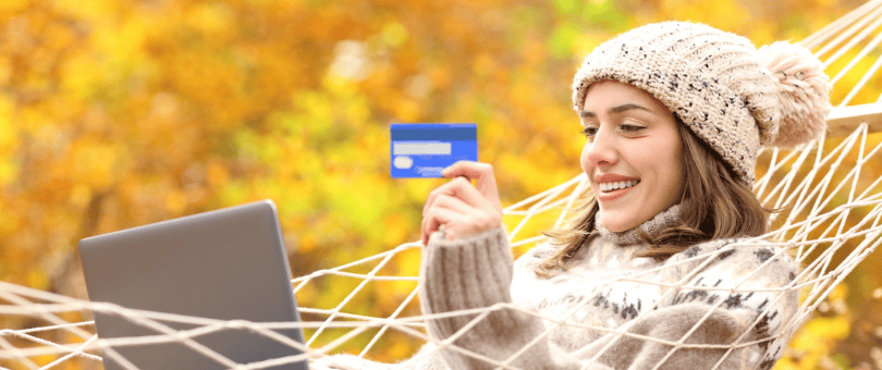 A woman in stocking cap and cozy sweater relaxed and shopping online in a hammock