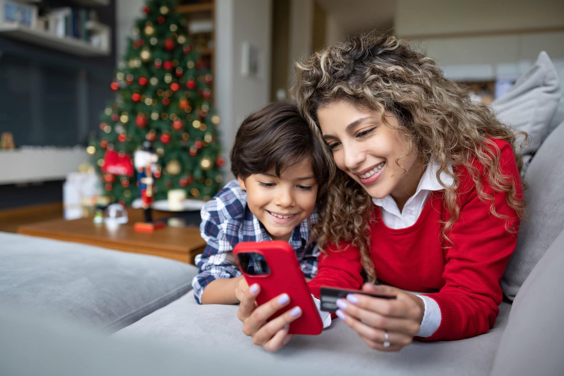 Happy mother and son shopping their Christmas presents online using her cell phone and paying by credit card – e-commerce concepts