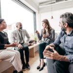 Group of sales people sitting in light-filled room dicussing sales strategy